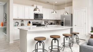 A modern kitchen with white cabinets, stainless steel appliances, a large island with stools, and pendant lighting.