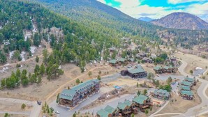 A lodge with multiple buildings, surrounded by forested mountains and a winding road.