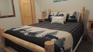 A bed with a forest-themed bedspread, a wooden headboard, and a 'be our guest' pillow.