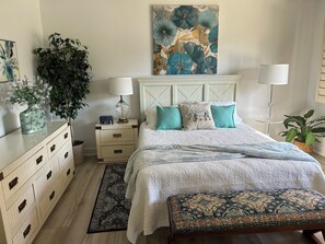 Una camera da letto con un letto, comodini, una cassettiera, un quadro di grandi dimensioni e una pianta in vaso.