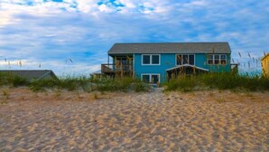 A beachfront house with a prominent blue exterior, a balcony, and a sandy beach in the foreground. - Toes in the Sand 🏖 Drink in Hand!  2 Decks, Views throughout, Great location! (Emerald Isle)