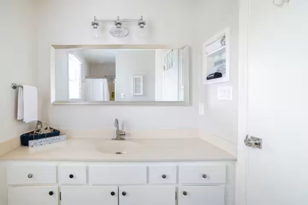 A bathroom with a white vanity, a sink, a mirror, and a towel rack.