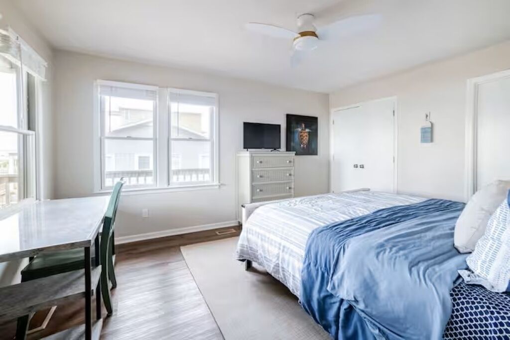 Un dormitorio con cama, cómoda, televisor y ventana.