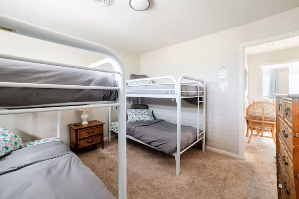 A room with bunk beds, a small wooden nightstand, a wicker chair, and a dresser.