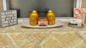 Un tocador de baño con artículos de aseo, incluyendo dos botellas de Acondicionador de Recuperación Pracaxi, un tarro de Exfoliante de Azúcar y Shea, y una pastilla de jabón Dove.
