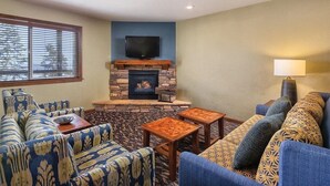 Ein Wohnzimmer mit Kamin aus Stein, blauen Sofas mit Muster und einem darüber montierten Fernseher.