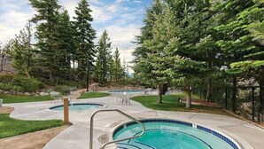 Ein Garten mit Schwimmbecken, umgeben von Bäumen und einer Terrasse mit Sitzgelegenheiten.
