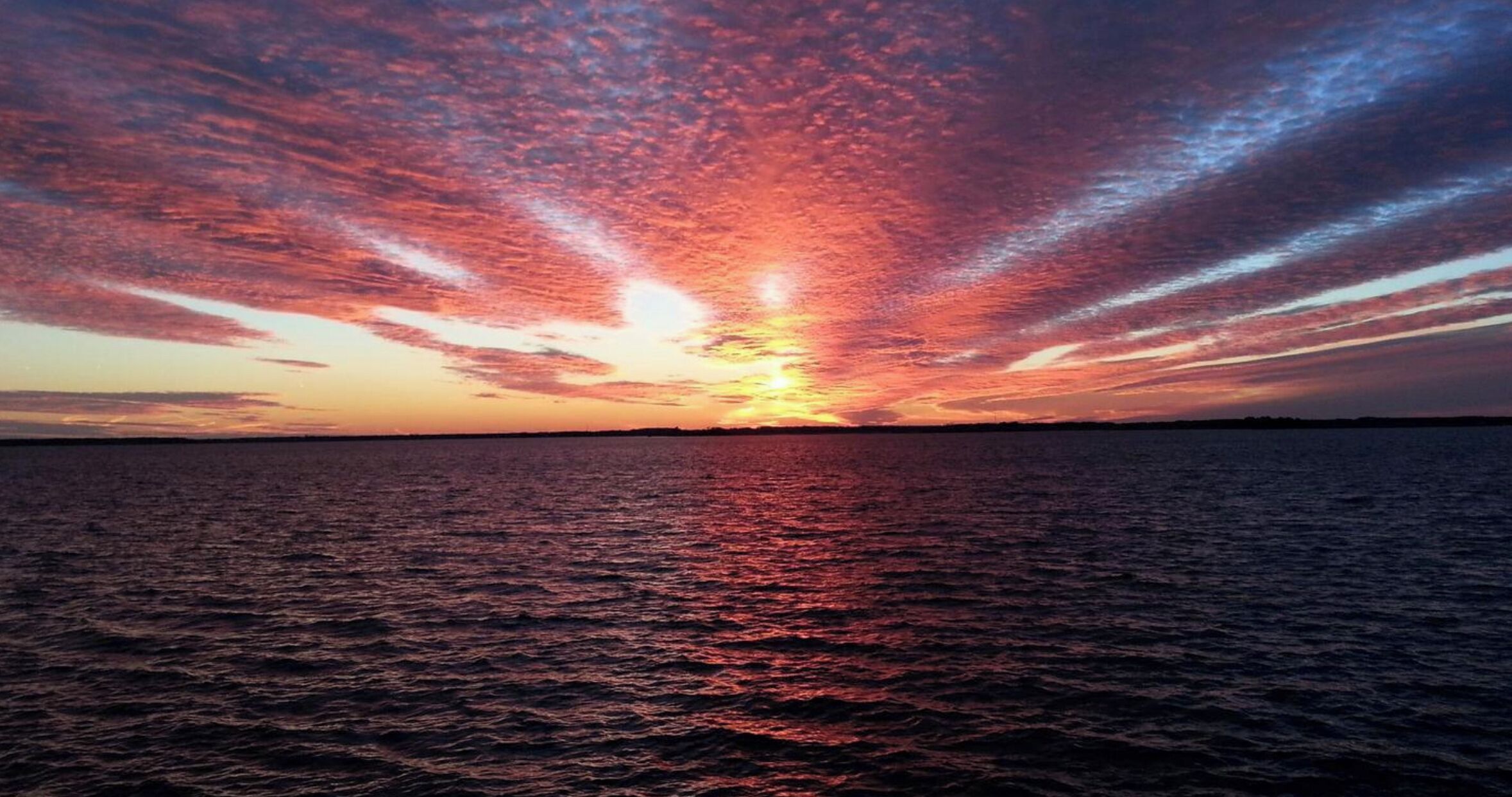 Un atardecer sobre un cuerpo de agua con un horizonte despejado.