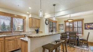 A kitchen with wooden cabinets, a granite countertop, and a bar area with stools. - Quiet - Spacious- On Ski Bus Line - Community Hot Tubs - WD (Steamboat Springs)