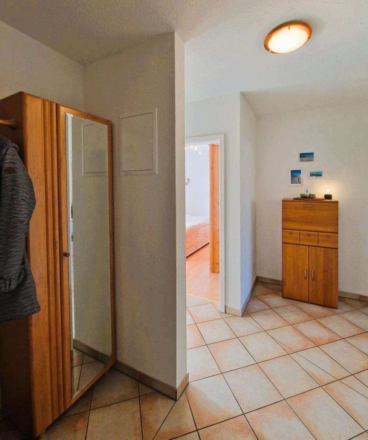 Una habitación con un armario de madera, un espejo, suelo de baldosas y una puerta que da a otra estancia.