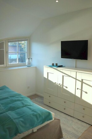 Une chambre à coucher avec un lit, une commode, une télévision et une fenêtre.