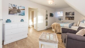 A cozy bedroom with a bed, a sofa, a dresser, and a TV.