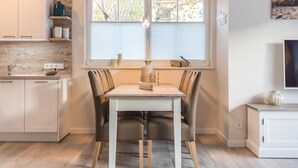 A modern kitchen with white cabinets, a dining table with chairs, and a window with blinds.