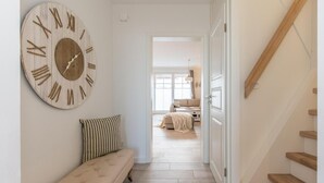 A hallway with a large wooden clock, a bench, and a staircase leading to another room.