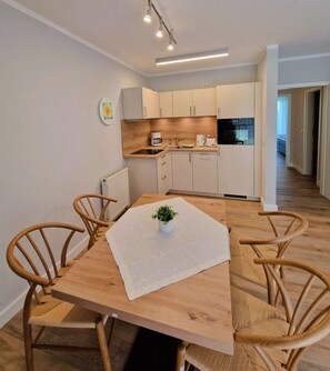 Une cuisine moderne avec des meubles blancs, une table à manger en bois et quatre chaises en osier.