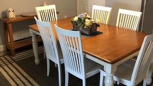 Comedor con una mesa de madera, sillas blancas, un centro de mesa floral y un tapete a rayas.