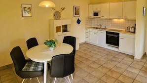 A compact kitchen with white cabinets, a dining table with four chairs, and a tiled floor.