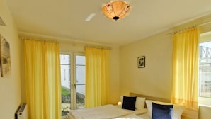 A bedroom with a double bed, two bedside tables, a small stool, a heater, and a window with curtains.
