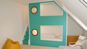 A room with a teal wall, two circular mirrors, a bed with white bedding, a yellow bean bag, and a grey sofa.