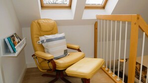 A room with a yellow leather chair, a wooden crib, and two skylights.