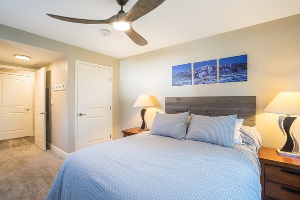 A bedroom with a bed, two bedside tables with lamps, a ceiling fan, and a door.