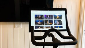 A stationary bike with a screen displaying workout videos, positioned in front of a wall with a mounted TV. - Honeymoon Suite (Elbow Cay)