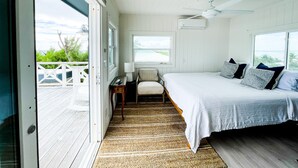 A bedroom with a bed, a desk, a chair, and a view of the outdoors. - Honeymoon Suite (Elbow Cay)