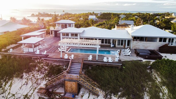 A beachfront property with a swimming pool, outdoor seating, and a wooden deck leading to a beach area. - Honeymoon Suite (Elbow Cay)