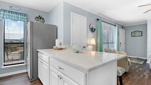 A kitchen with a white island, a refrigerator, and a window with blinds. - Seahorse 512- Seahorse Condos (Gulf Shores)