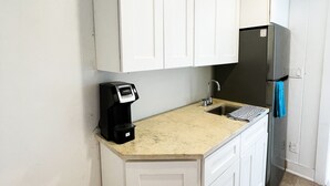 A compact kitchen with white cabinets, a stainless steel refrigerator, a coffee maker, and a sink. - Ocean front loft. (Elbow Cay)