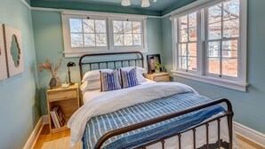 Ein Schlafzimmer mit Bett, Nachttischen, einem Fenster und einer Kristallleuchtre.'