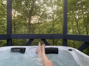A hot tub with a wooden deck and a forest view.