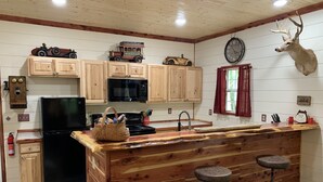 Una cocina con armarios de madera, un refrigerador negro, una isla de madera con taburetes, un reloj y una cabeza de venado montada.