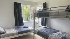 A dormitory room with bunk beds, a window with curtains, and a carpeted floor. - The Bach on Dorset 🌊 (Opunake)
