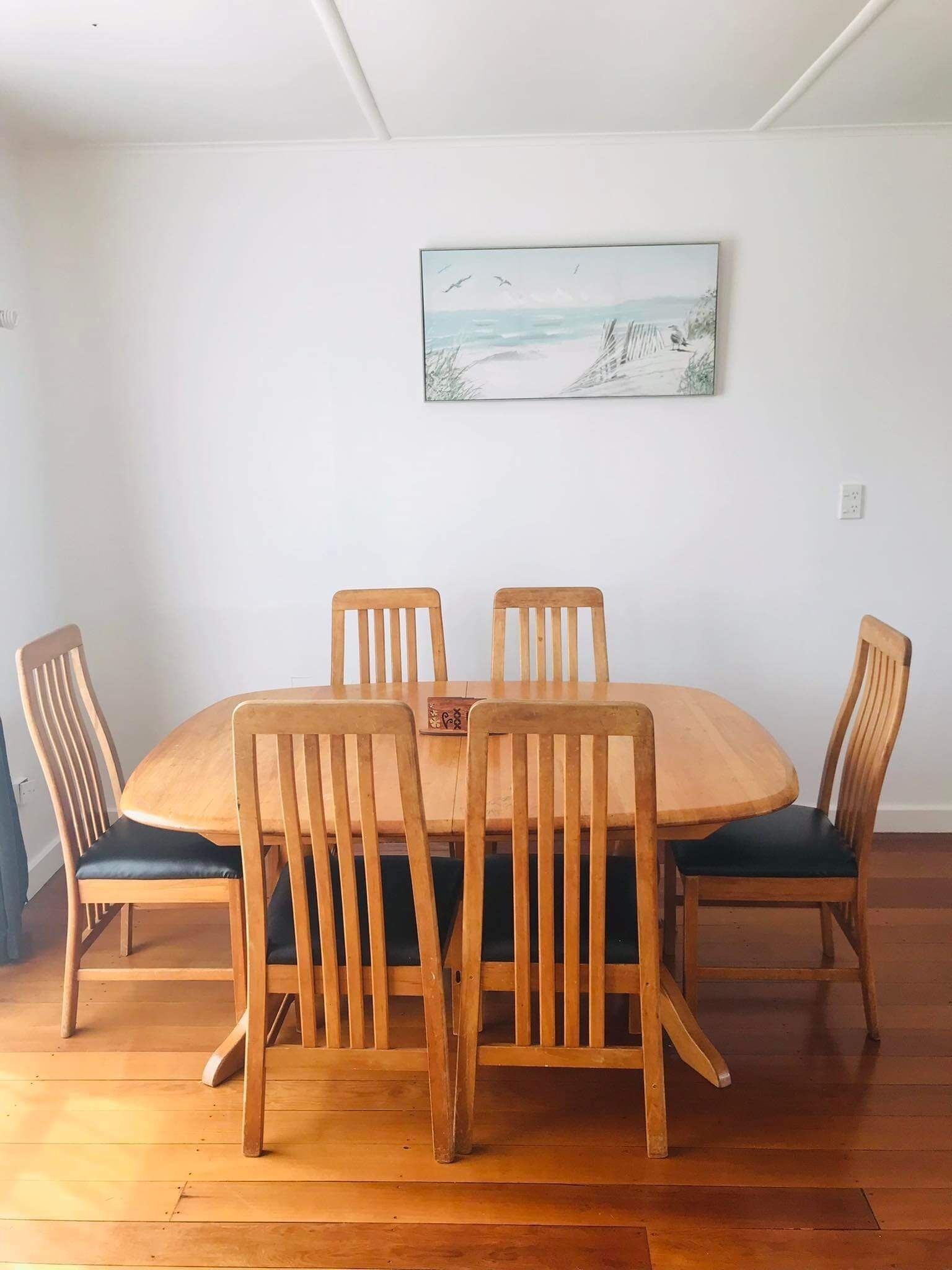 Un coin repas avec une table et des chaises en bois, un tableau au mur et un plafond blanc.