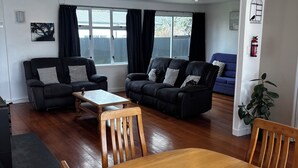 A modern living room with two black sofas, a wooden dining table, and a blue sofa in the background. - The Bach on Dorset 🌊 (Opunake)