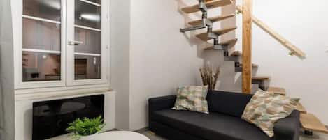 Ein Wohnzimmer mit einem schwarzen Sofa, einem weißen Couchtisch, einem Fernseher und einer Wendeltreppe.