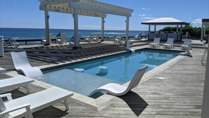 Uma área de piscina com espreguiçadeiras, um pérgola e vista para o oceano.