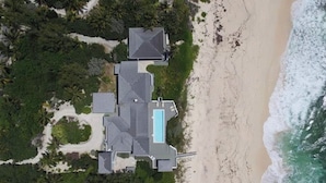 Vista aérea de uma propriedade à beira-mar com piscina, vários edifícios e vegetação exuberante.
