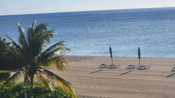 A beach with palm trees, a sandy shore, and two umbrellas. - Silver Sand Villa 7A (Cotton Ground)