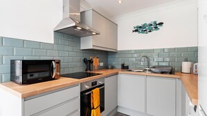 A compact kitchen with a microwave, oven, and sink. - 25 Coedrath Park - Sea Views From Balcony Short Walk to Beach Parking (Saundersfoot)