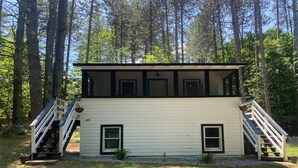 A two-story cabin with a white exterior and black trim, featuring a front staircase and a small porch area. - Newfound Lake Cozy Cottage (Bristol)