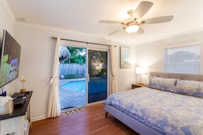 A bedroom with a bed, a ceiling fan, a nightstand, a TV, and a sliding glass door leading to a pool area.
