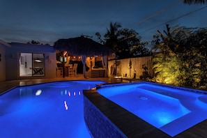 A swimming pool with a thatched-roof structure and a wooden fence.