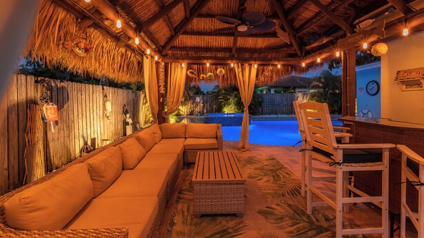 Un rincón tranquilo con techo de paja, muebles de mimbre y una piscina al fondo.