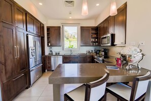A modern kitchen with dark wood cabinets, stainless steel appliances, and a central island with chairs.