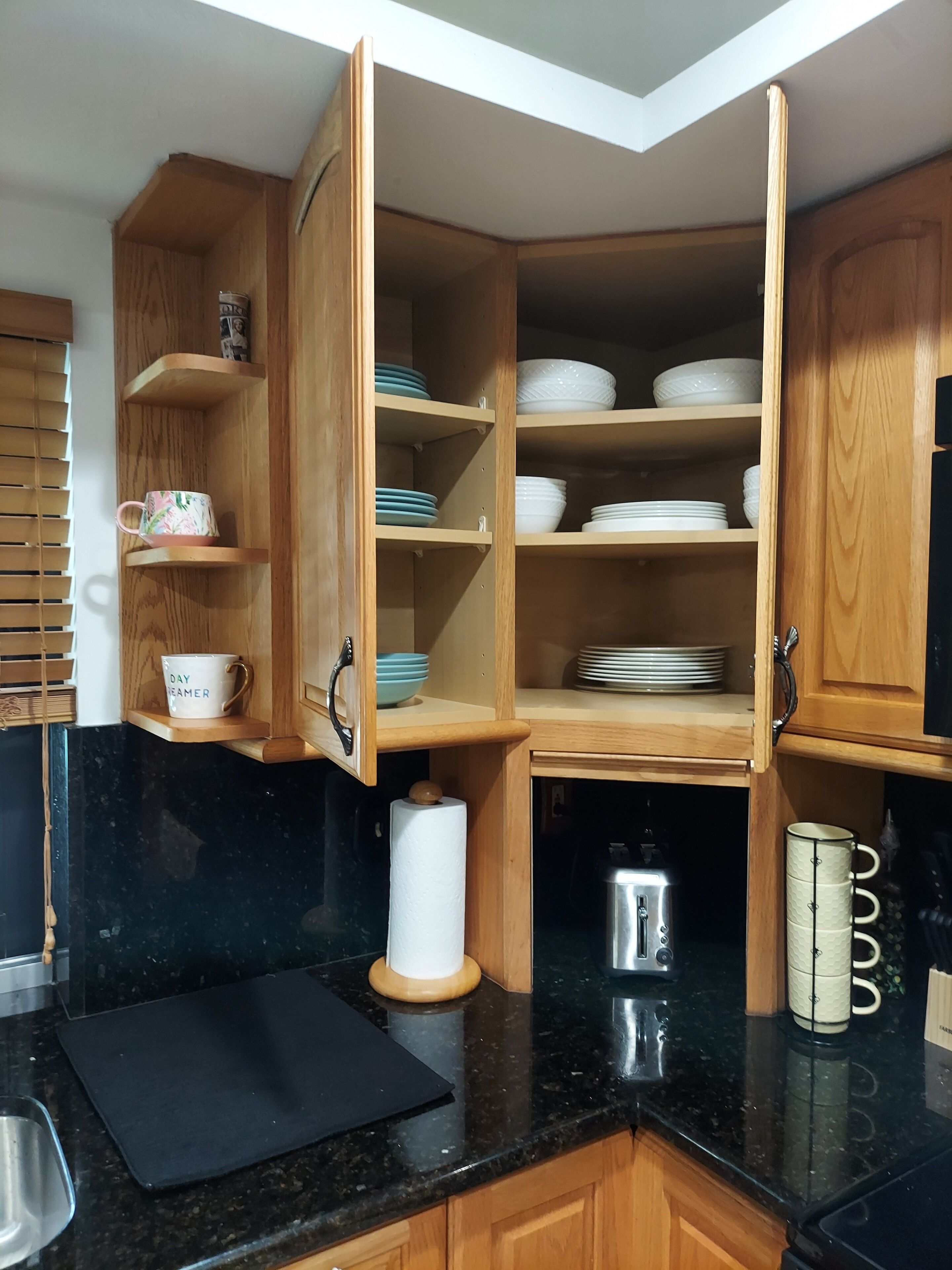 A kitchen with wooden cabinets, black countertops, and a variety of dishes and utensils.