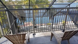 Varanda com duas cadeiras de madeira e guarda-corpo de metal, com vista para um corpo de água.