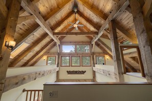 Ein Innenraum mit hohen Holzwänden, einem zentralen Ventilator, großen Fenstern und einer Treppe.