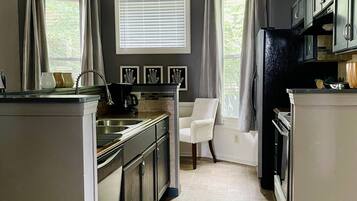 A modern kitchen with a central island, stainless steel appliances, and a window with blinds.